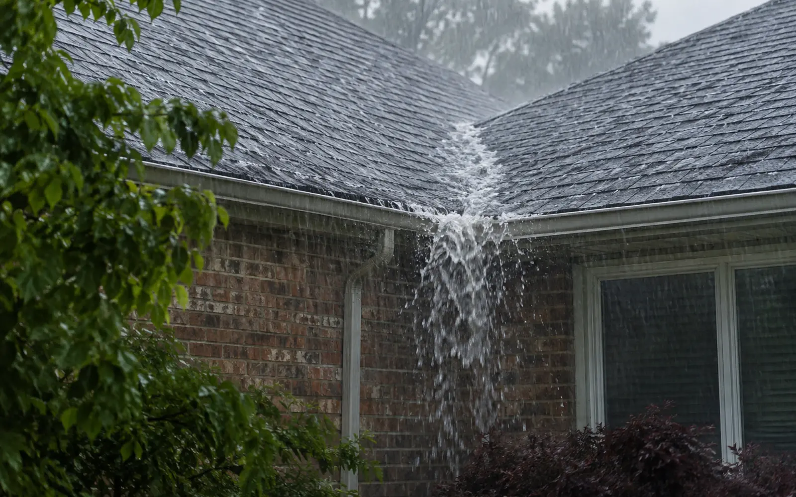 Heavy rain overflowing an eavestrough below a roof valley